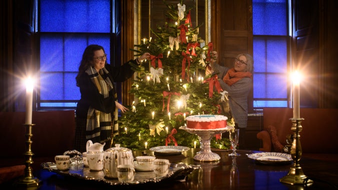 Two members of staff adjusting a Christmas tree behind a table laid out with a tea set and cake